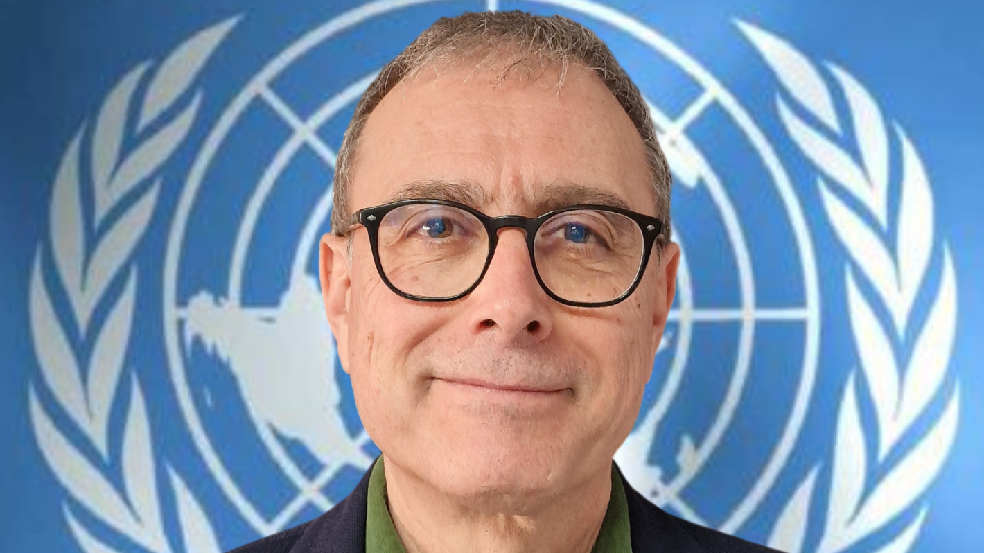 A headshot of a man in glasses in front of a UN logo