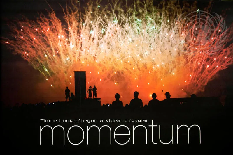 Silhouetted figures watch colorful fireworks light up the night sky in Timor-Leste, with the words "Timor-Leste forges a vibrant future – momentum" overlaid on the image.