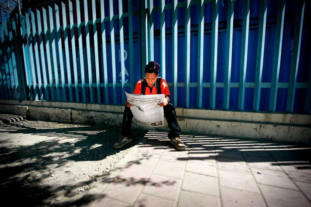 Young man reading a newspaper in Dili.