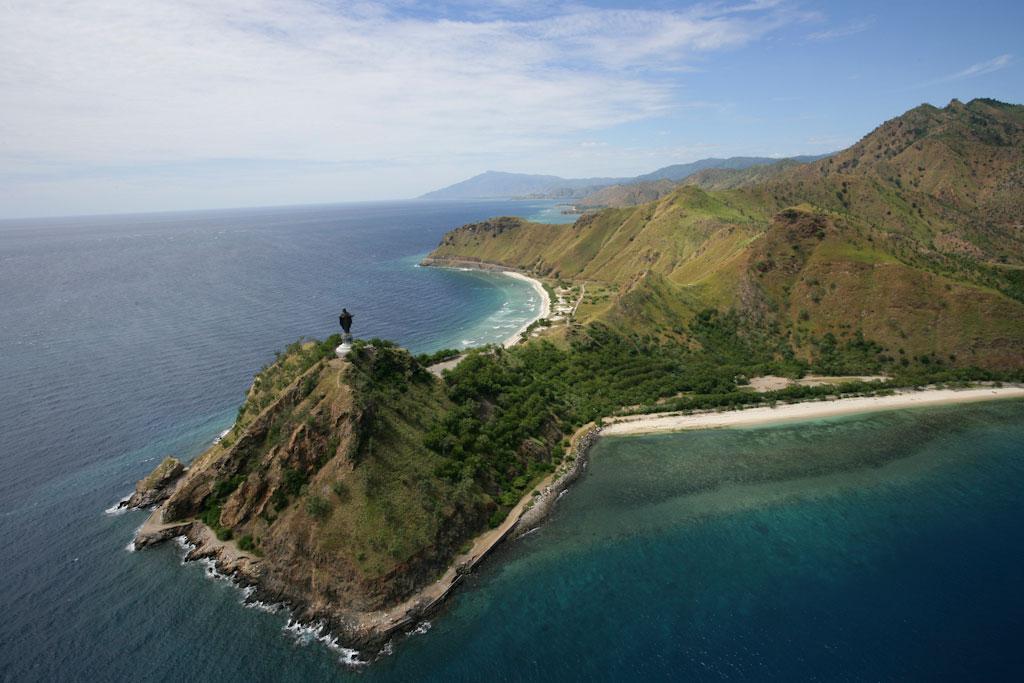 Aerial view of a peninsula surrounded by water and covered in lush, greenery. Atop the peninsula is a statue or memorial.