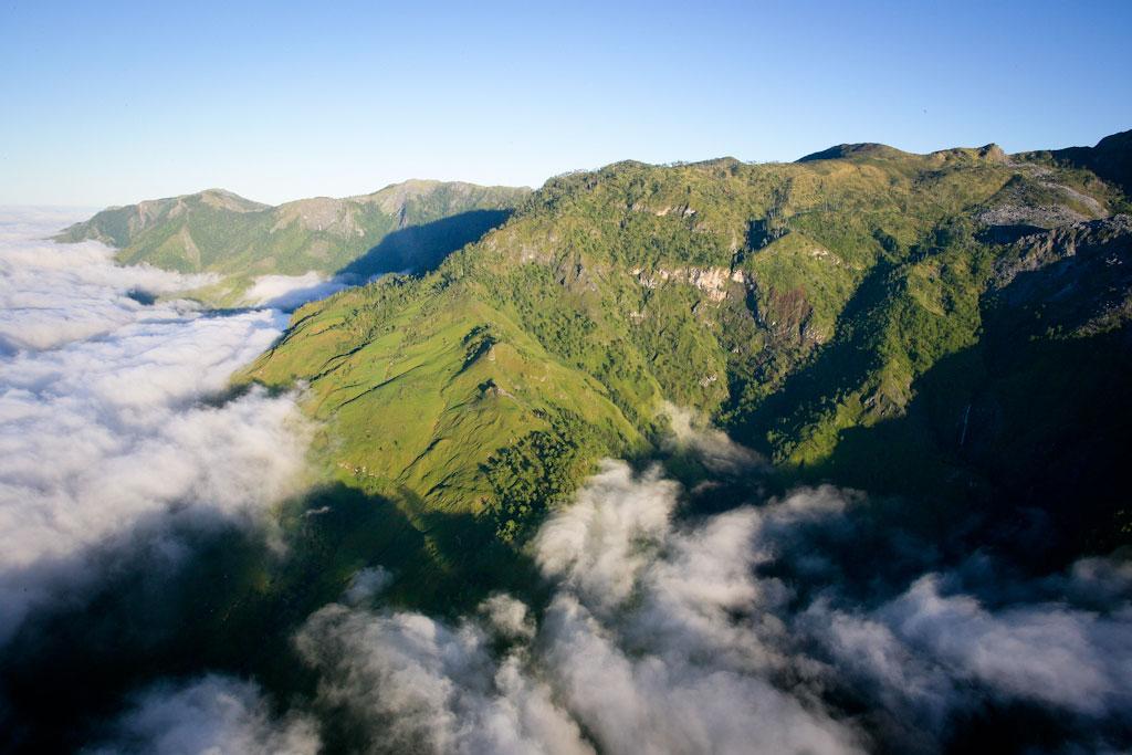 Aerial view of Mount Ramelau. The mountain is covered in lush greenery with clouds surrounding it. 