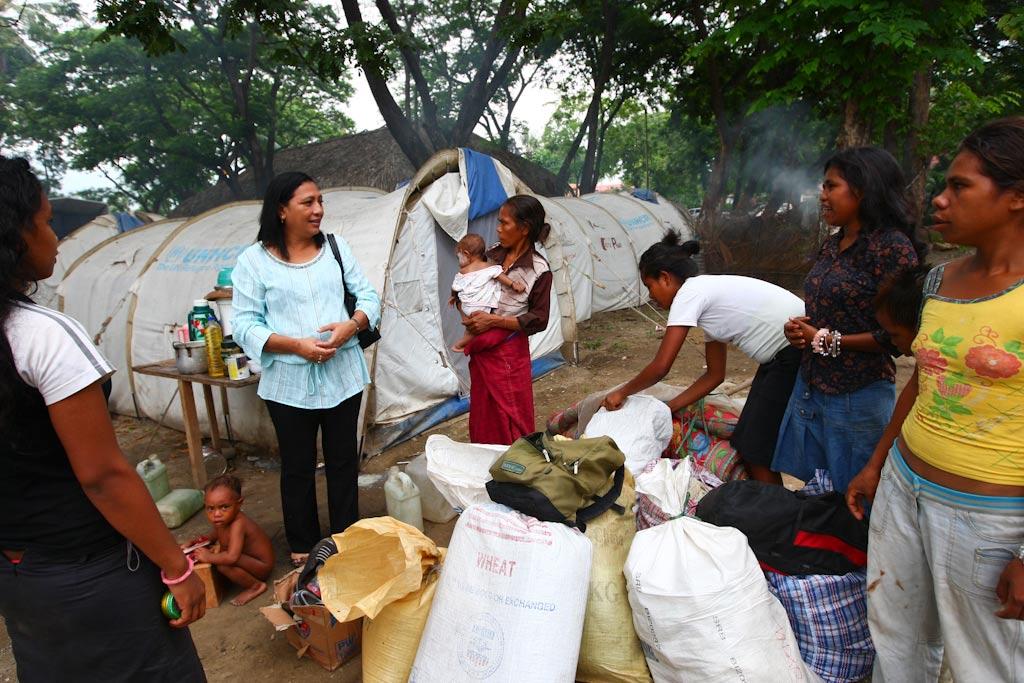 A woman in a blue shirt representing the United Nations speaking with a group of women in an Internally displaced persons (IDPs) camp. In the background is an UNHCR tent.